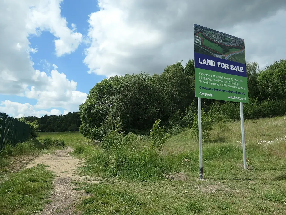 A land for sale board on a grass plot at the edge of a wood