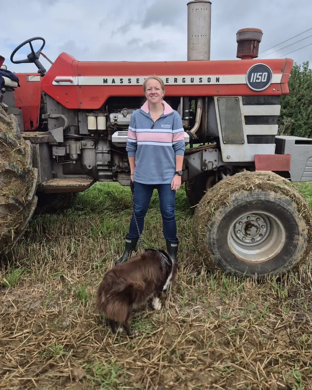 Milly Barker in wellies beside a Massey Ferguson tractor, with her collie